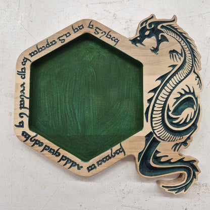 A top-down view of a hexagonal 11 by 10.5 inch solid hardwood dice rolling tray featuring a carved border with a dragon and fantasy runes, crisp hand-painted green accents, and a matching green flocked velvet center.