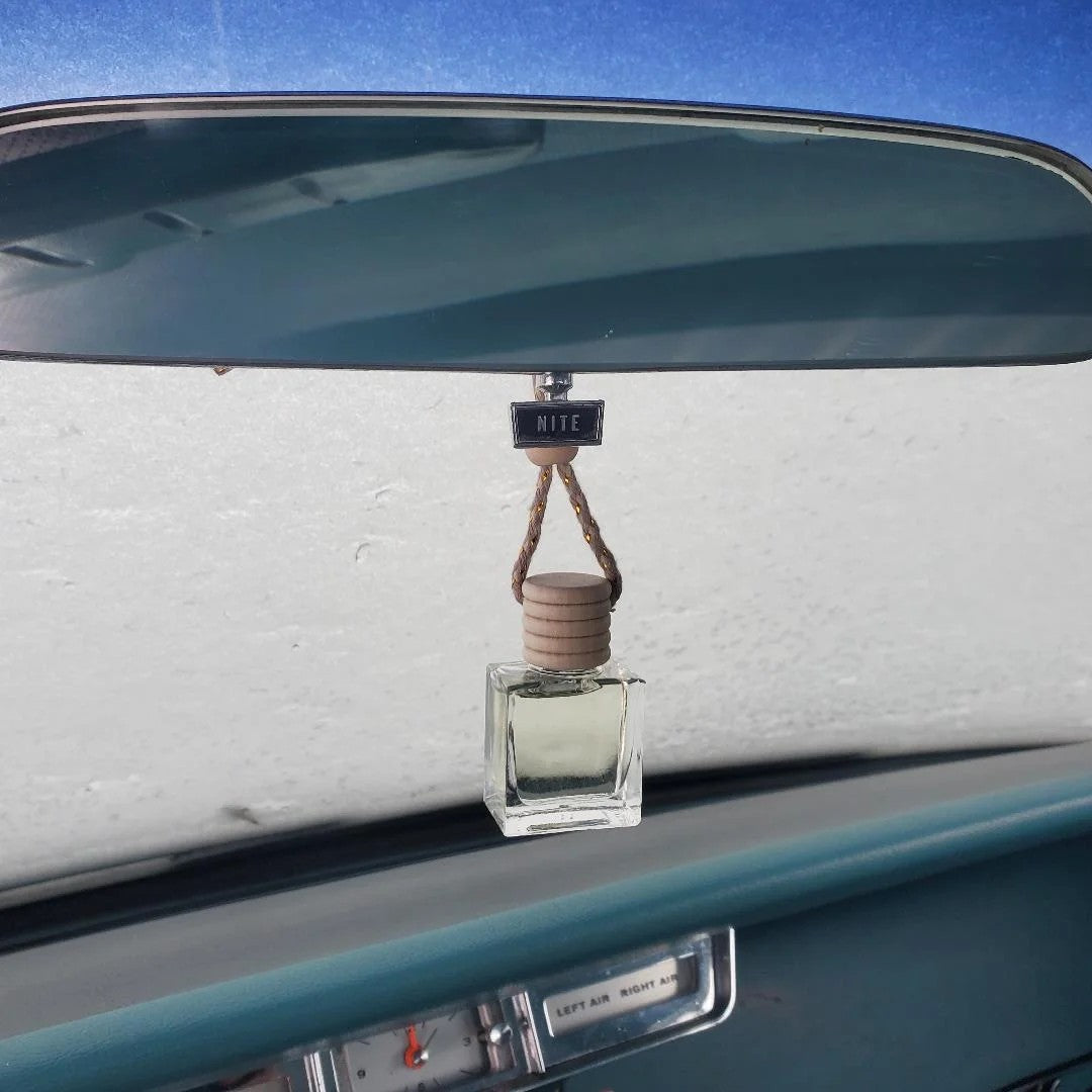 Hanging glass car diffuser with a wooden cap suspended from a vintage vehicle's rearview mirror.