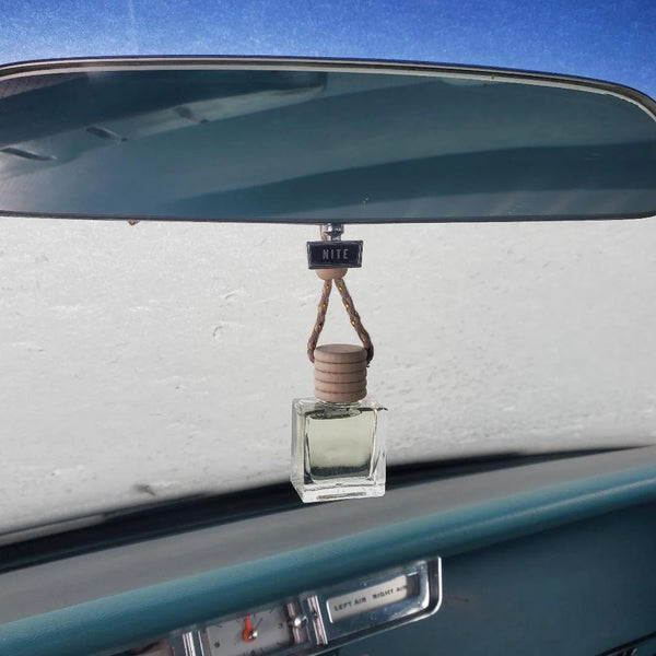 Hanging glass car diffuser with a wooden cap suspended from a vintage vehicle's rearview mirror.