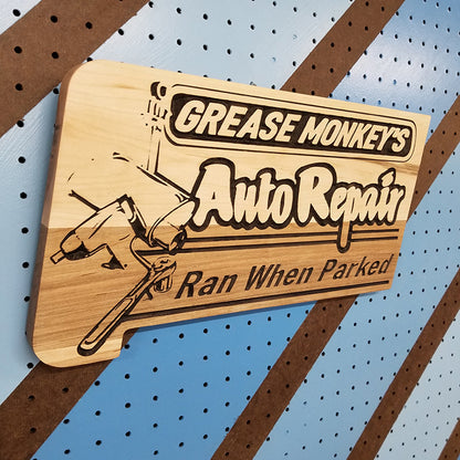Angled shot of a Handcrafted relief-carved hardwood sign featuring the text "Grease Monkey's Auto Repair: Ran When Parked"