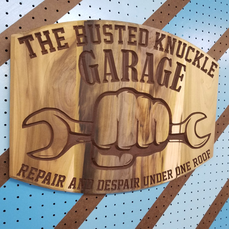Angled shot of a Relief carved hardwood sign featuring the text: "The Busted Knuckle Garage: Repair and Despair Under One Roof."