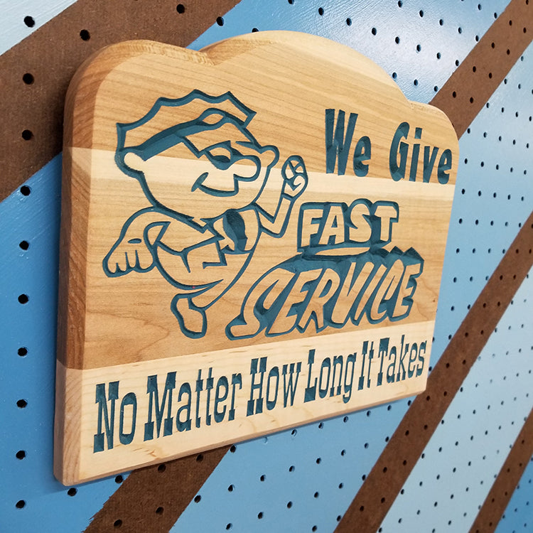 Angled shot of a relief carved hardwood sign featuring a cartoon mechanic and text: We Give Fast Service No Matter How Long It Takes.