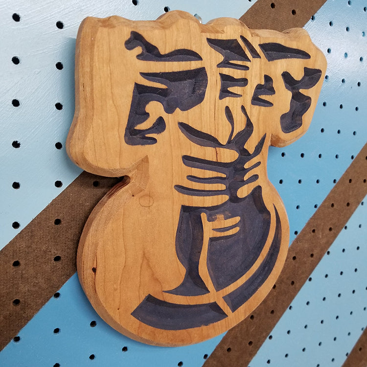 Angled shot of a relief carved hardwood sign in the shape of the historic Liberty Bell, featuring a detailed yoke and clapper design with blue paint.