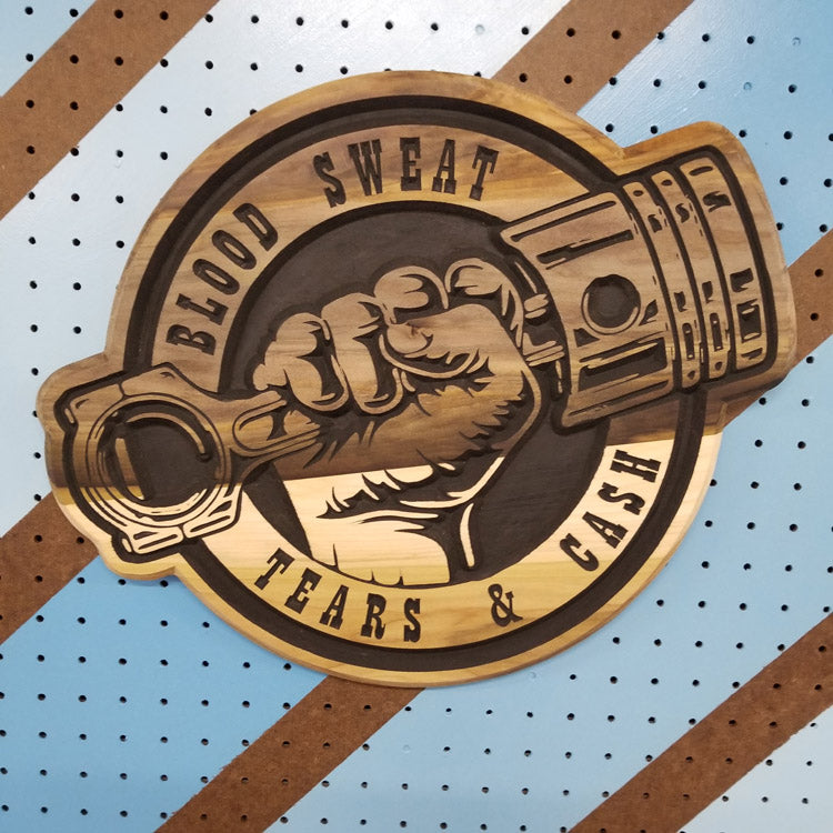 Relief carved hardwood sign with brown painted piston fist design and Blood Sweat Tears & Cash text on a striped pegboard.