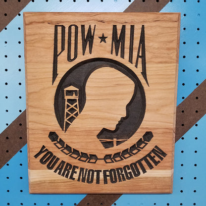 Relief carved hardwood POW MIA sign with a silhouette design and You Are Not Forgotten text on a striped pegboard.
