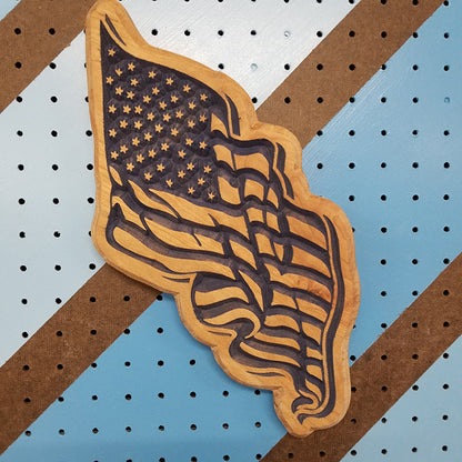Relief carved hardwood American flag sign with a waving, rippled design on a striped pegboard.