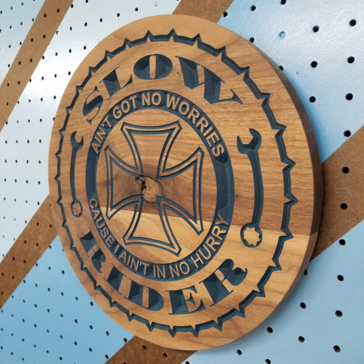 Angled shot of a relief carved hardwood Slow Rider biker sign with cross and wrench details on a blue pegboard