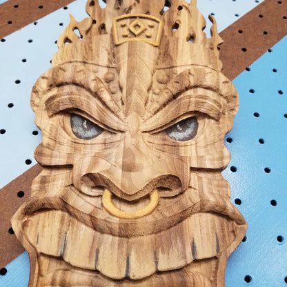 Close-up shot of a 3D relief carved hardwood Tiki totem sign with unique hand-painted details on a blue pegboard.
