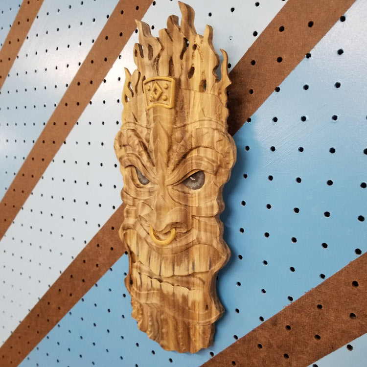 Angled shot of a 3D relief carved hardwood Tiki totem sign with unique hand-painted details on a blue pegboard.