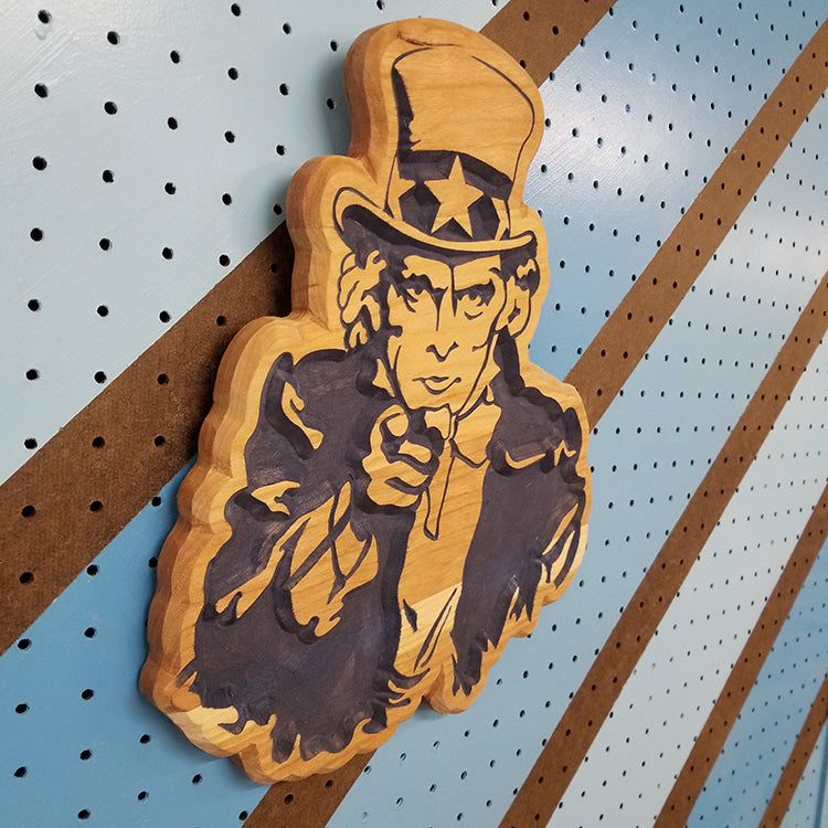 Angled shot of a custom hardwood Uncle Sam patriotic garage sign with carved Americana relief design on a blue pegboard.