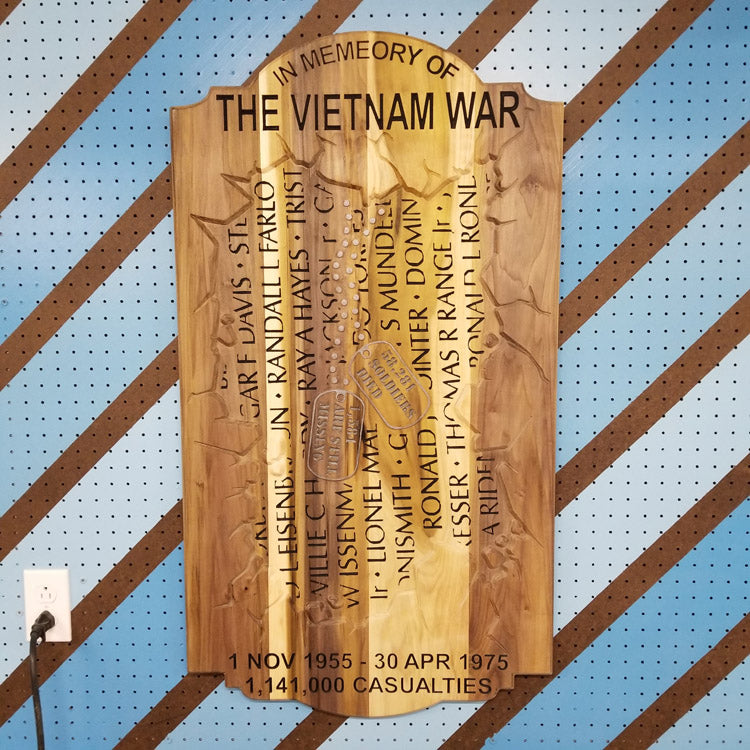 Custom hardwood Vietnam War memorial sign with carved service member names and casualty count on a pegboard.