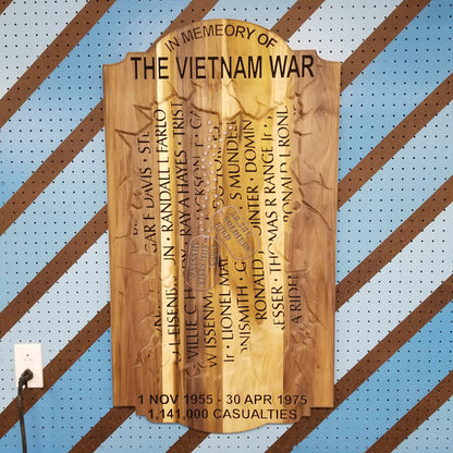 Custom hardwood Vietnam War memorial sign with carved service member names and casualty count on a pegboard.