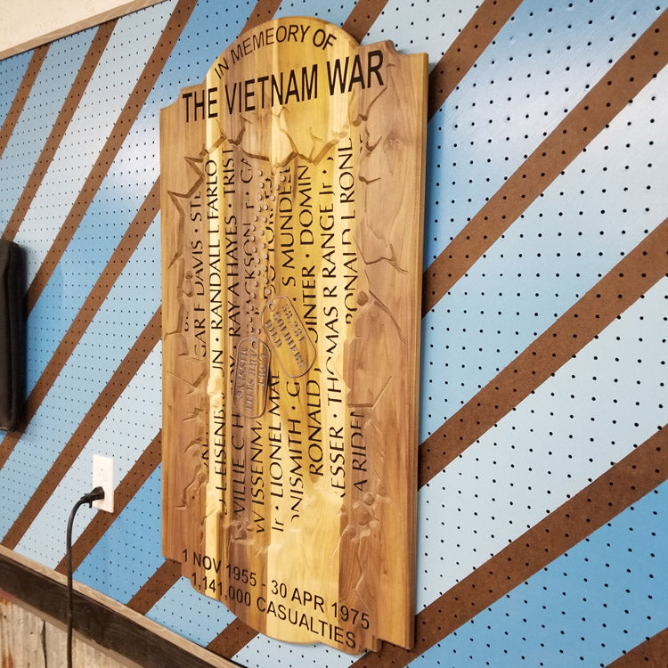 Angled shot of a custom hardwood Vietnam War memorial sign with carved service member names on a blue pegboard.