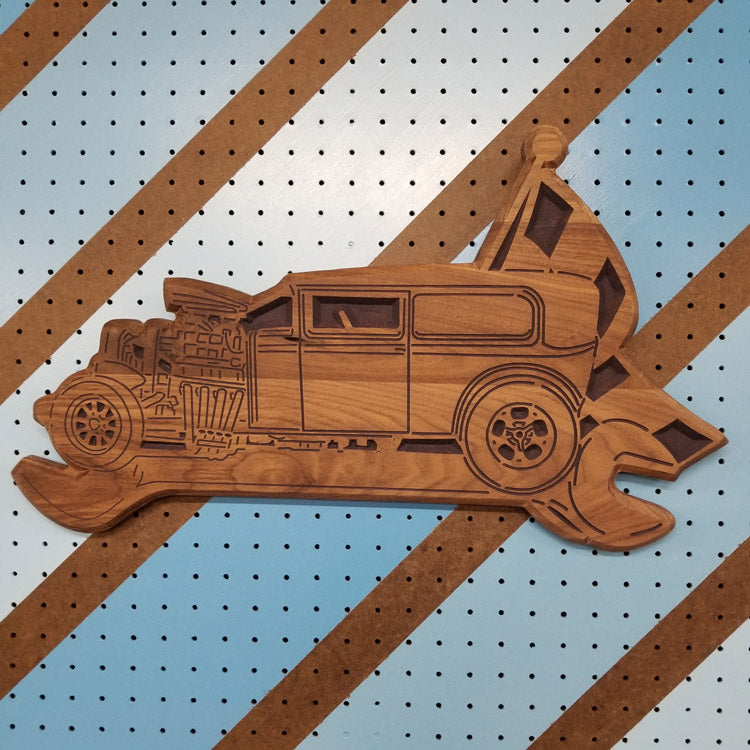 Custom hardwood wrench flag sign with an intricate vintage car relief carving on a shop pegboard.