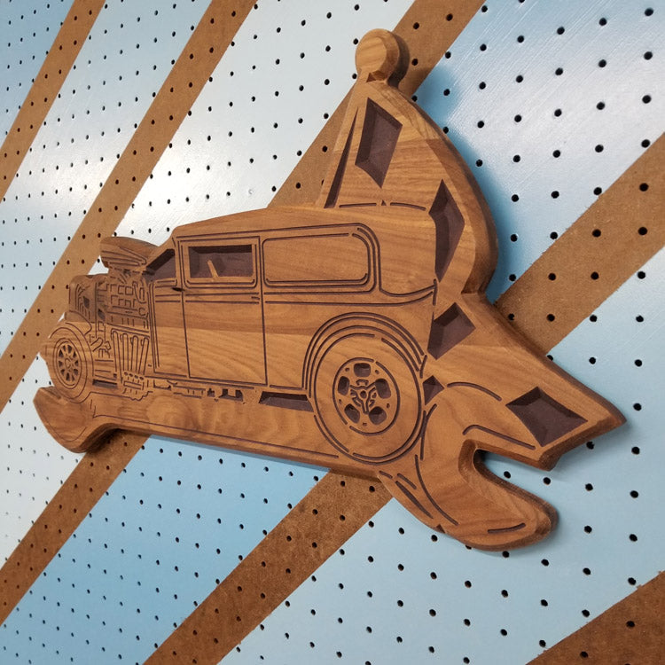 Angled isometric shot of a custom hardwood wrench flag garage sign with detailed hot rod carving on pegboard.
